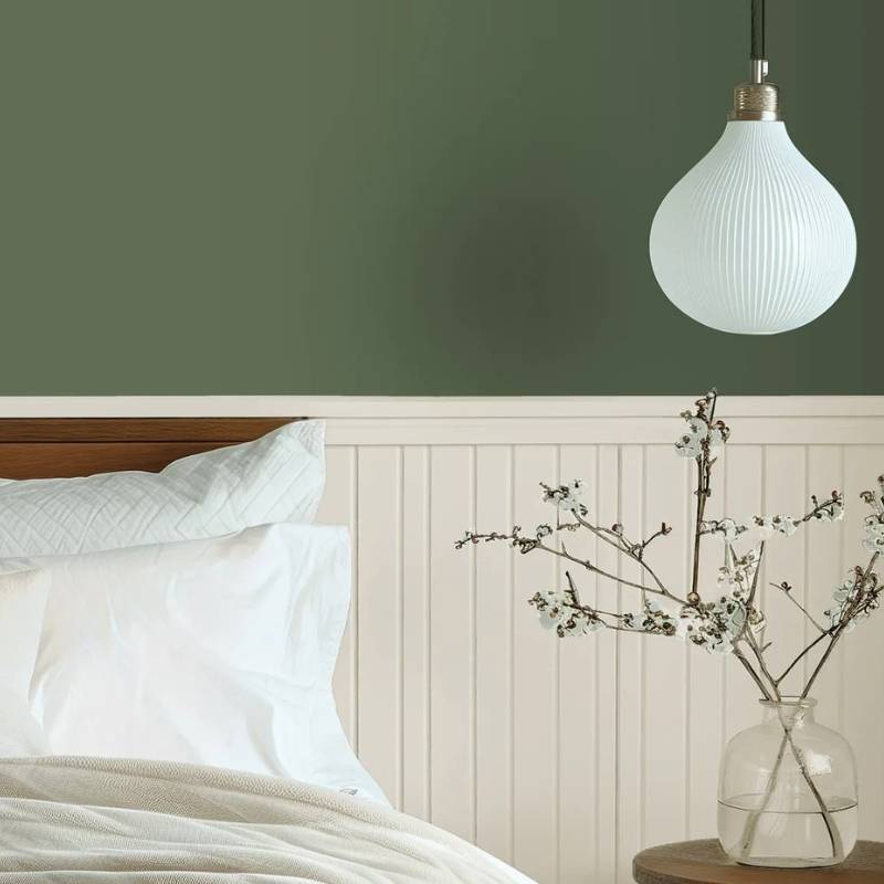 Dunn-Edwards Midnight Garden DE5657 deep mossy green paint color on a bedroom wall with white bedding and warm neutral wainscoting